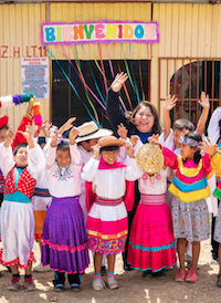 A woman and group of children smiling in front of a church.